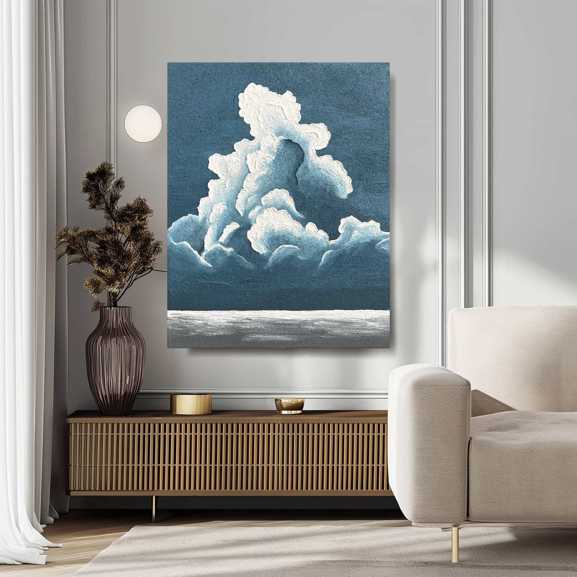 "BILLOWY CLOUDS: Hand-painted Portrait shaped abstract textured wall art painting depicting a large cloud in the sky, with a blue and white colour palette, hanging in a cozy corner of the living room."