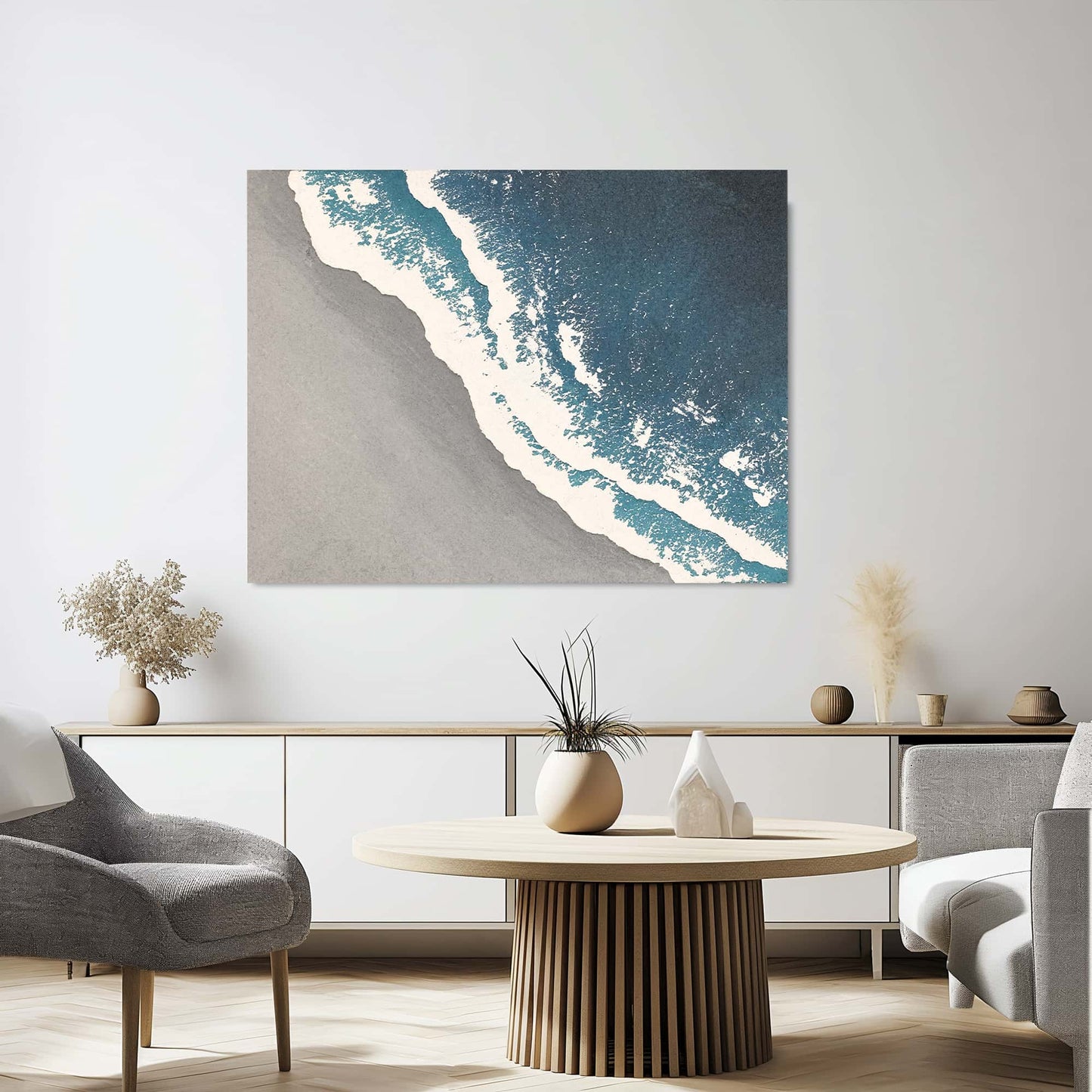 "SEASIDE, STYLE A: Hand-painted Landscape shaped textured wall art painting depicting a grey beach, white waves crashing on the grey shore, and the azure sea, in shades of blue, white, grey, and navy, hanging on the wall in the living room."