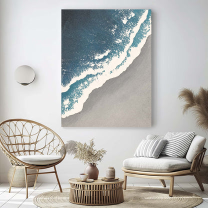 "SEASIDE, STYLE A: Hand-painted Portrait shaped textured wall art painting depicting a grey beach, white waves crashing on the grey shore, and the azure sea, in shades of blue, white, grey, and navy, hanging on the wall in the lounge."